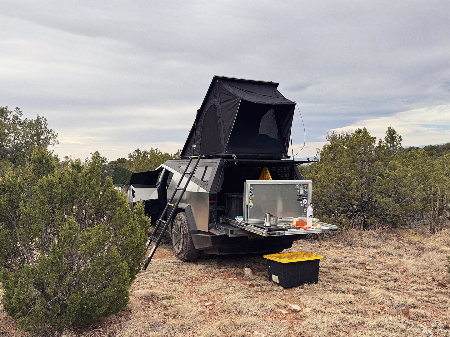 Cybertruck camper with a rooftop tent, bed slide, and camp kitchen in a natural setting